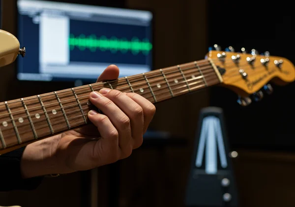 Hand on guitar fretboard with metronome on screen